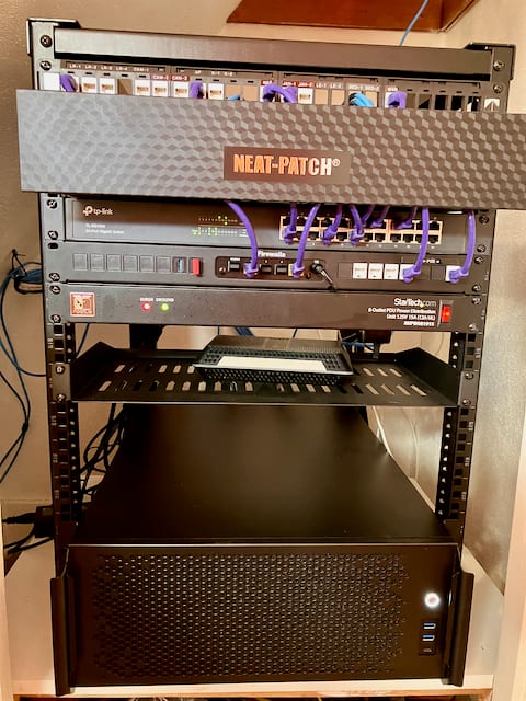 The finished rack: a patch panel behind a cable manager at the top, a 24-port switch wired with purple patch cables, a firewall appliance, a rack PDU, a vented shelf, and the completed 4U server at the bottom.