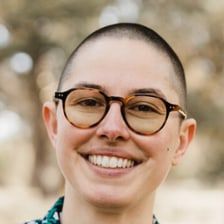 Bailey, smiling, in round tortoiseshell glasses and a floral shirt.